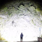 Person in hoodie illuminated by powerful auto LED spotlight against rocky hill, night scene