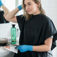 Woman applying hair dye at home wearing gloves and black cape, with clarioy hair care products