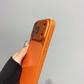 Hand holding orange iPhone case, premium phone accessory from clarioy