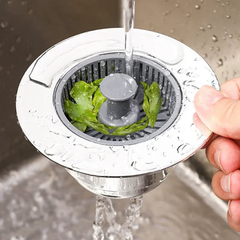 Hand holding a sink strainer with leafy debris under running water, kitchen homeware at clarioy
