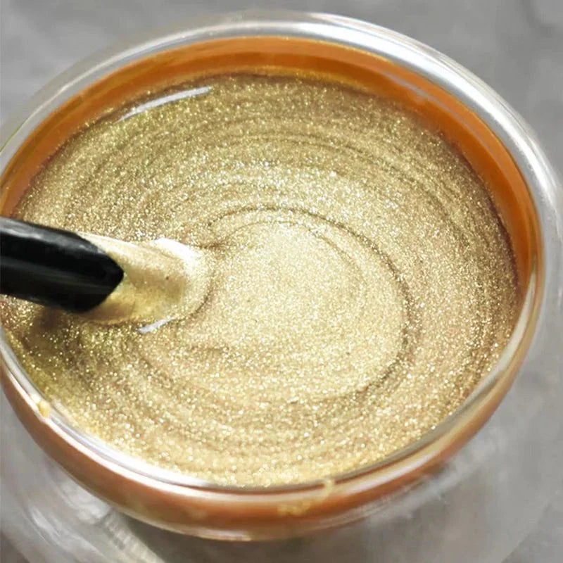 Close-up of gold glitter paint or gel in a clear jar, with a black spatula stirring, clarioy homeware.